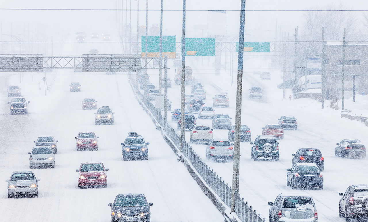 Heavy rush-hour traffic on a highway during a snowstorm with reduced visibility and slick conditions